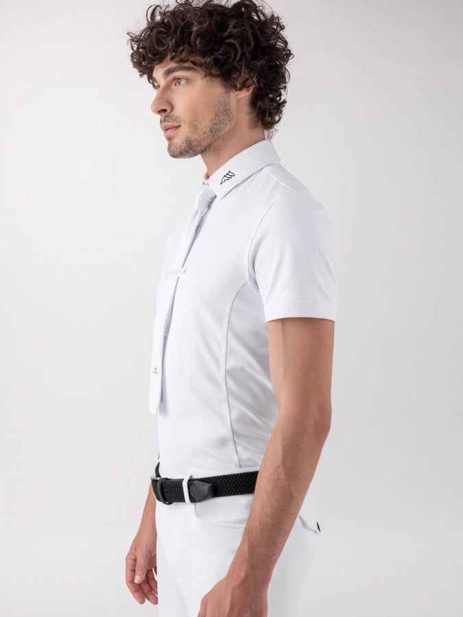 A man in profile wearing a white short-sleeve polo shirt, white trousers, and a black belt, photographed against a clean light gray studio background.