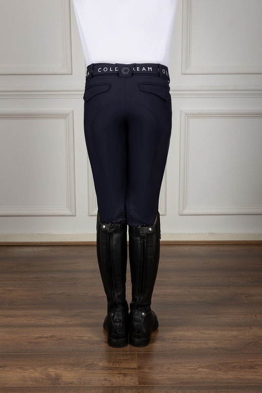 Person wearing navy riding pants with a white top and black riding boots on a wooden floor.