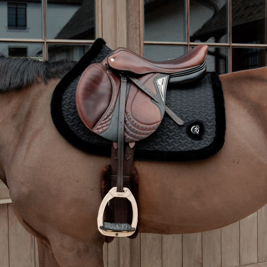 Brown leather saddle on a horse with a wooden stable background