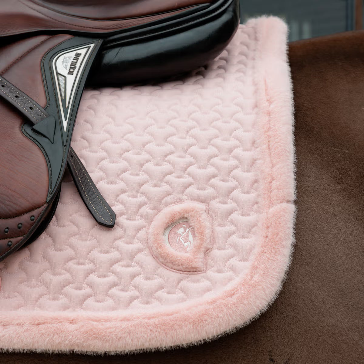Detail of a pink saddle pad on a brown horse