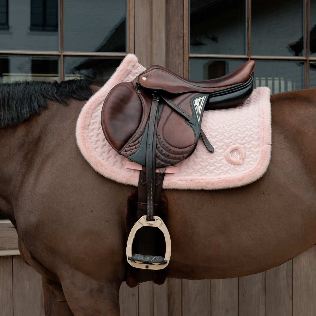 Horse with a brown saddle and pink pad on a wooden stable background