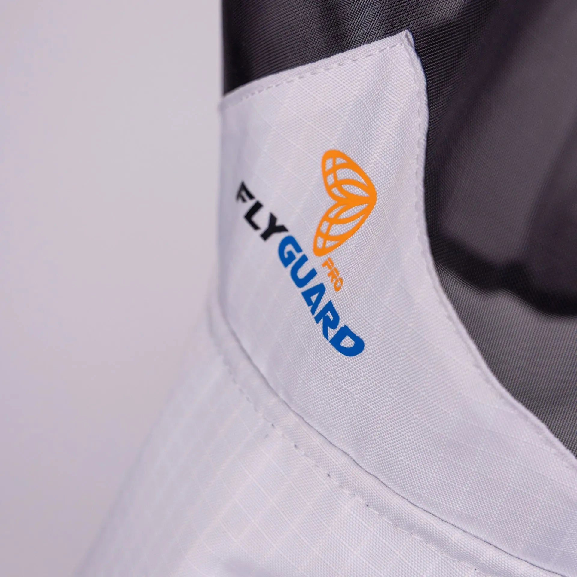 Close-up of a white garment with 'FlyGuard' logo on a light gray background
