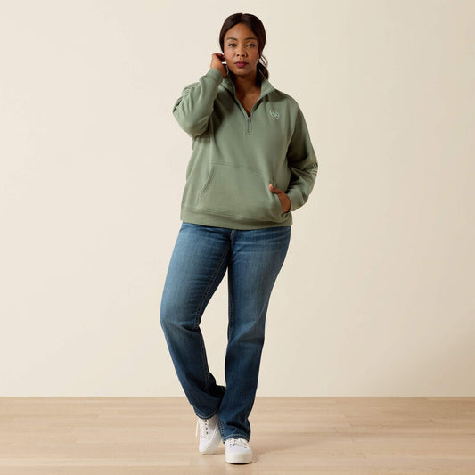 Woman wearing a green pullover and blue jeans against a beige background