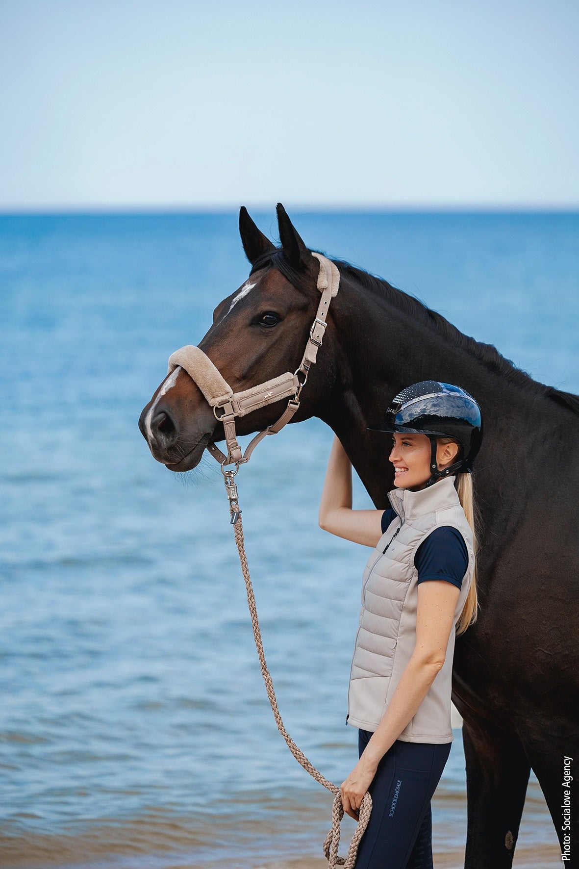Woman with a horse on a beach with blue water and sky