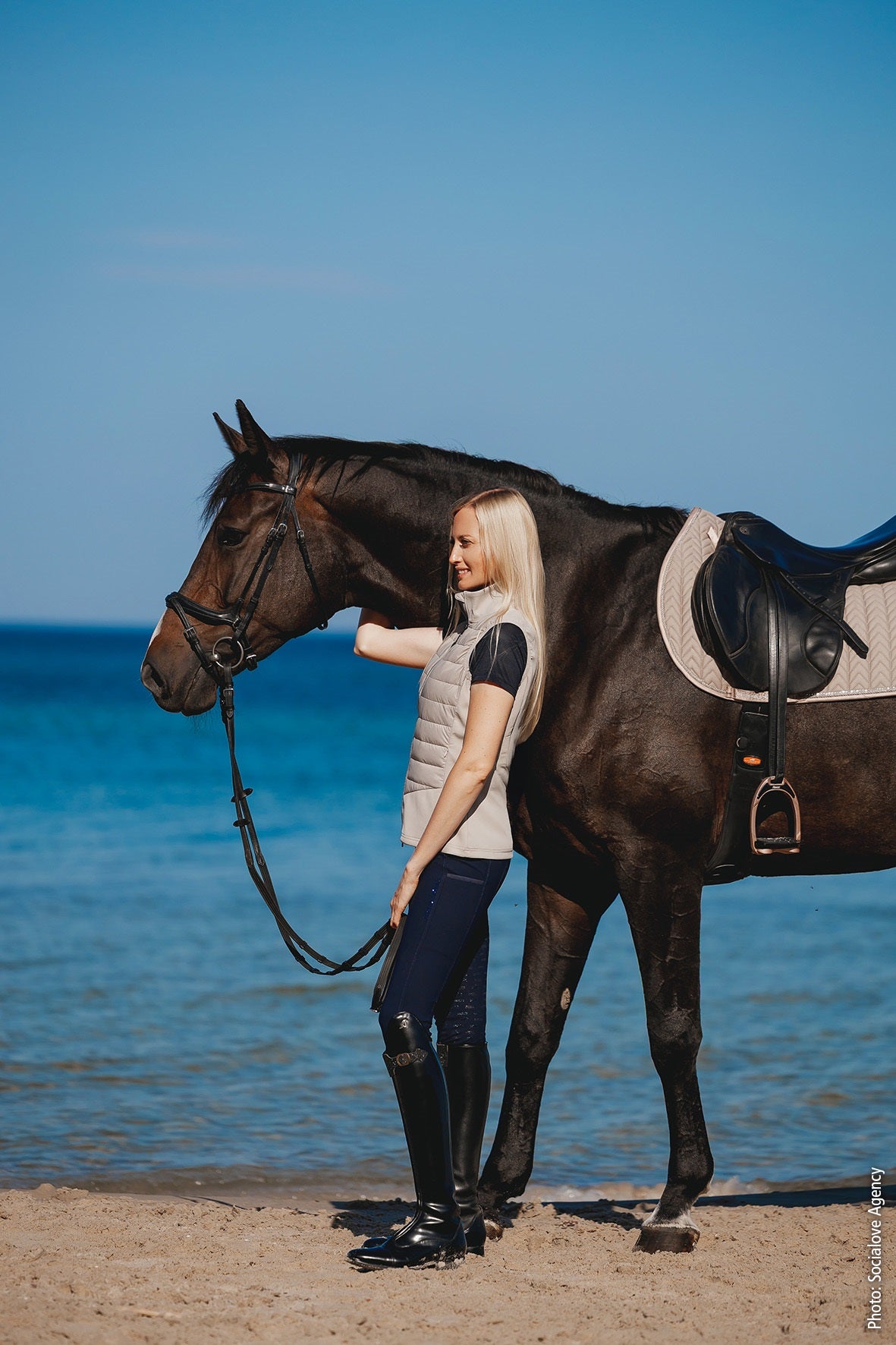Woman holding a horse on a beach