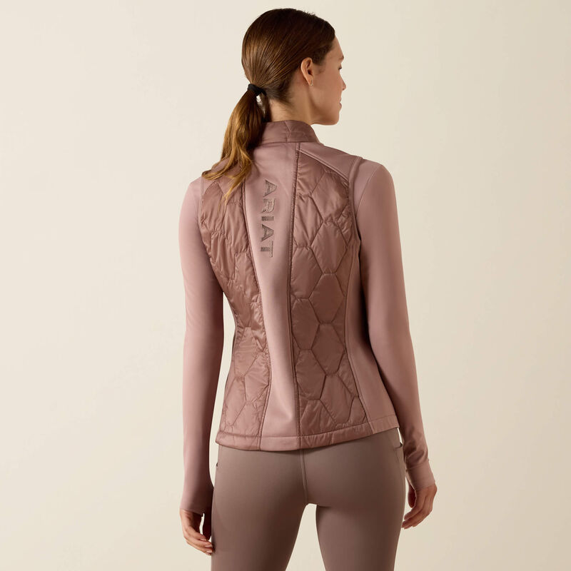 Woman wearing a pink quilted vest with 'Ariat' branding on a beige background