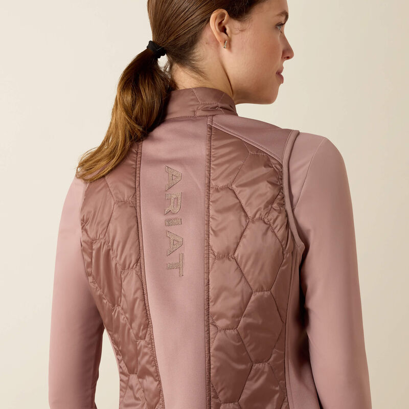 Person wearing a pink quilted jacket with 'Ariat' branding on a beige background