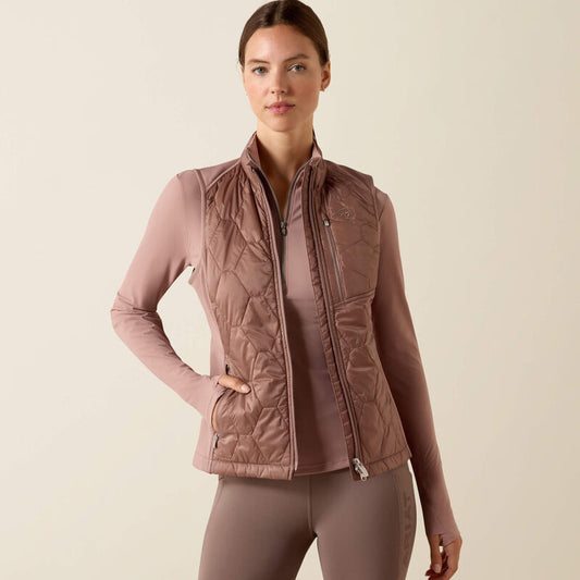Woman wearing a quilted vest over a long-sleeve shirt on a beige background