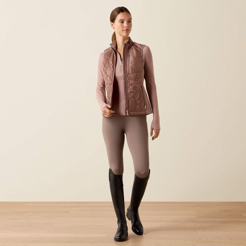 Woman wearing a pink quilted jacket, leggings, and black boots on a beige background
