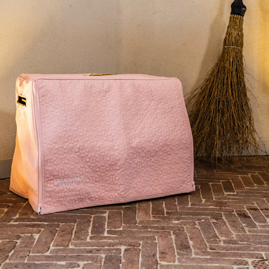 Pink quilted bag with a broom in the background on a brick floor.