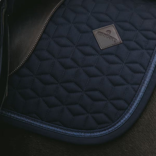 Close-up of a quilted navy blue saddle pad with a brand logo on a dark background