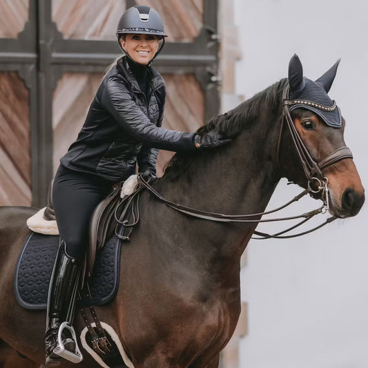 Woman riding a horse in equestrian gear with a neutral background