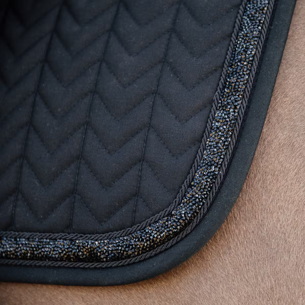 Close-up of a black quilted saddle pad with decorative trim on a brown surface.