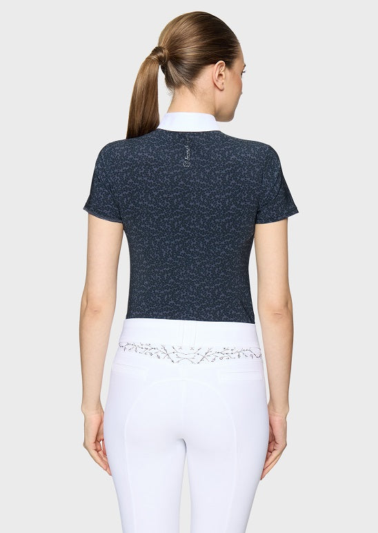 A woman shown from the back wearing a dark navy short-sleeve athletic top with a textured pattern and a white high collar, paired with white riding breeches.