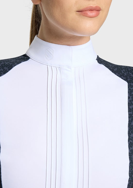 Close-up of a woman wearing a white high-neck riding shirt with vertical pleats and dark patterned shoulder panels.