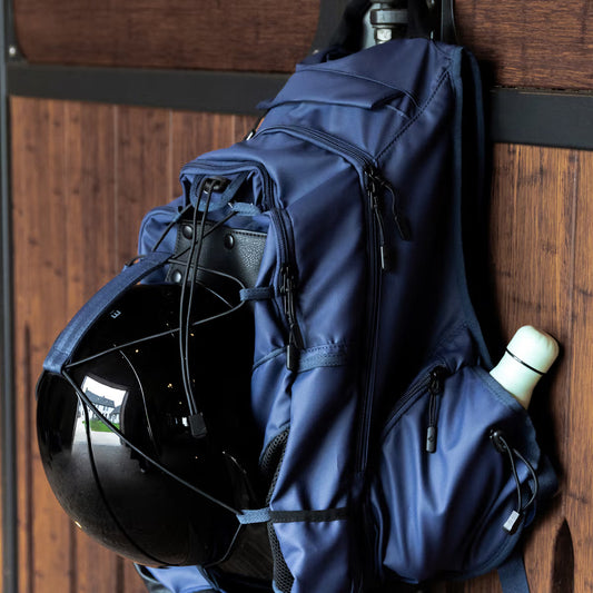 Blue backpack with a helmet and water bottle attached, hanging on a wooden door.