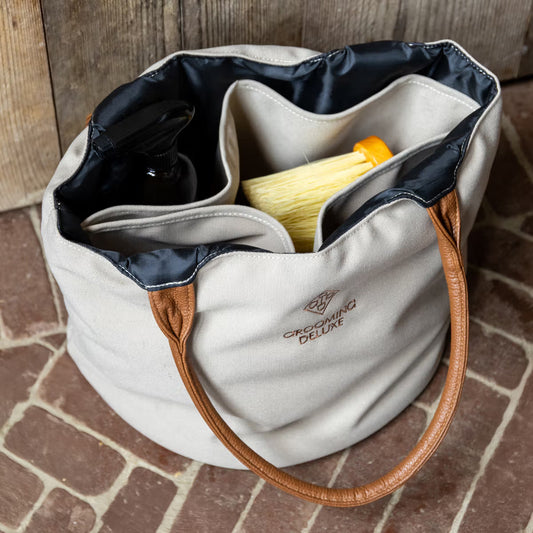 Beige tote bag with brown handles on a brick surface, containing grooming products.