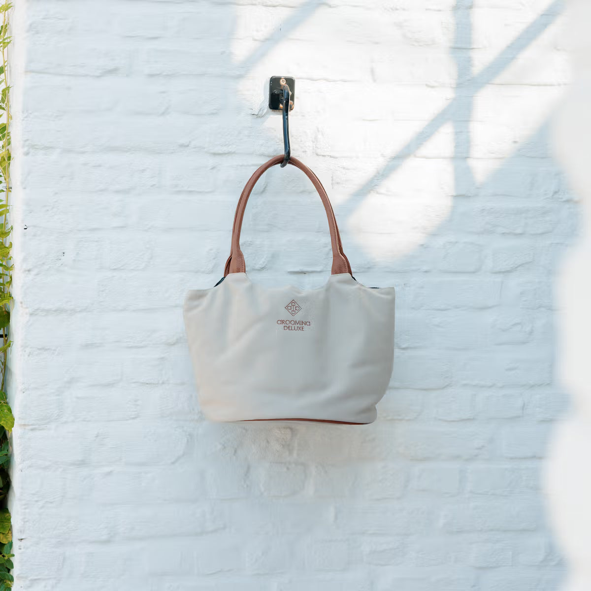 Beige tote bag with brown handle hanging on a white brick wall
