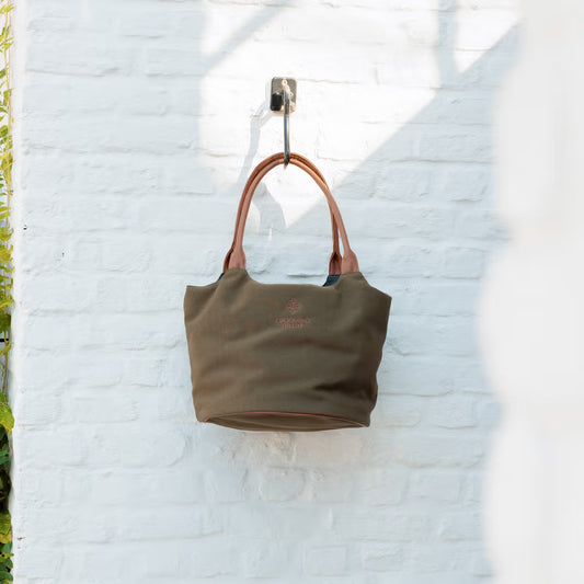 Green handbag with brown handles hanging on a white brick wall.