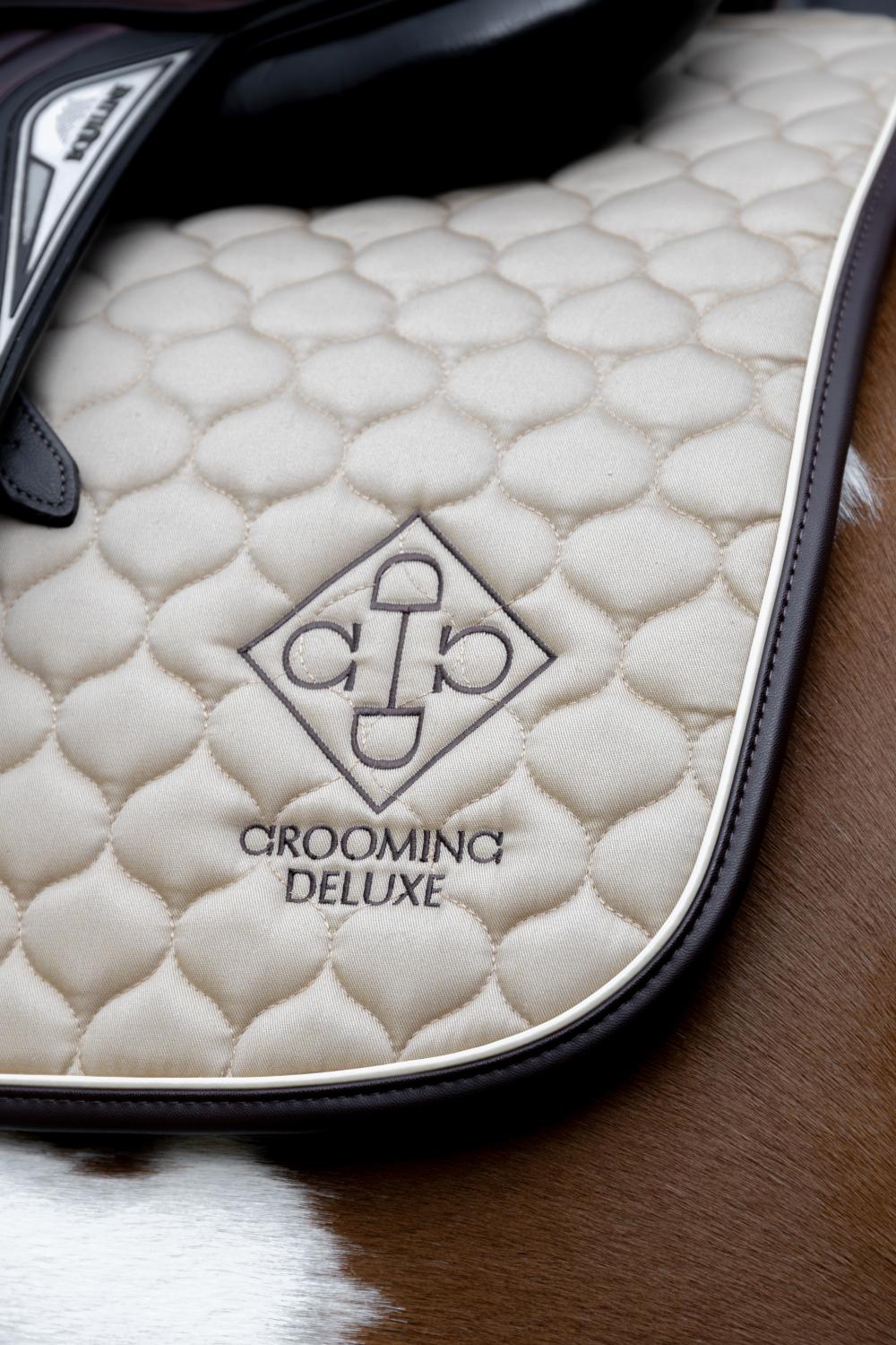 Close-up of a quilted saddle pad with 'Grooming Deluxe' branding on a horse's back.