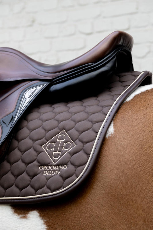 Brown leather saddle with 'Cromo Grooming Deluxe' logo on a horse.