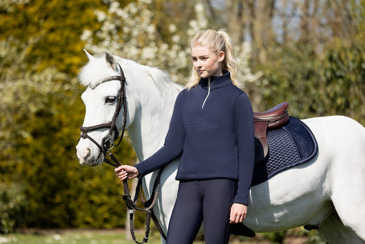 Woman in a navy blue outfit standing next to a white horse outdoors.
