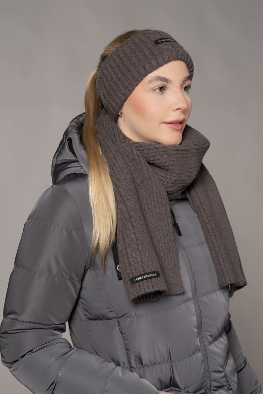 Woman wearing a gray winter coat, brown knit headband, and scarf against a neutral background