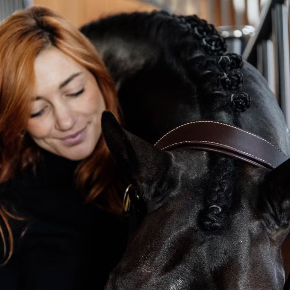 Woman with red hair petting a black horse wearing a headcollar
