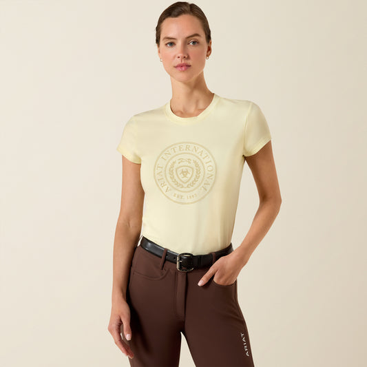 Woman wearing a light yellow t-shirt with a logo and brown pants on a beige background
