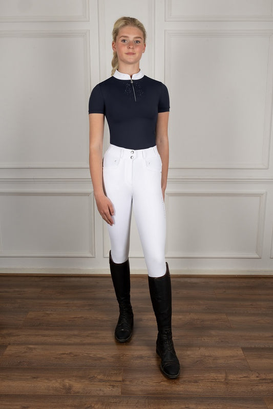 Person wearing equestrian attire including a navy top, white pants, and black boots against a plain background.