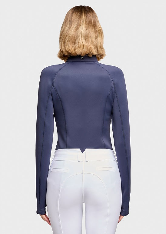 Rear view of a model wearing a navy blue long-sleeve mock neck riding shirt and white breeches against a solid white background.