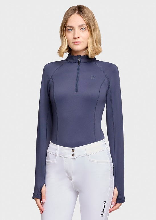 A woman modeling a navy blue long-sleeve quarter-zip equestrian shirt with white breeches against a solid white background.