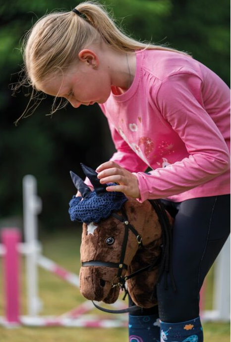 Child in pink shirt interacting with a toy horse outdoors