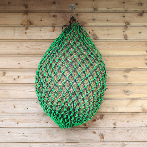 Green hay net bag filled with hay hanging on a wooden wall.