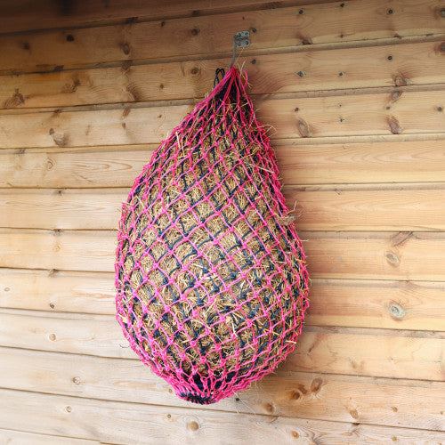 Pink net bag filled with hay hanging on a wooden wall
