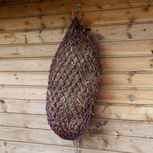 Rainbow haynet filled with hay hanging on a wooden wall