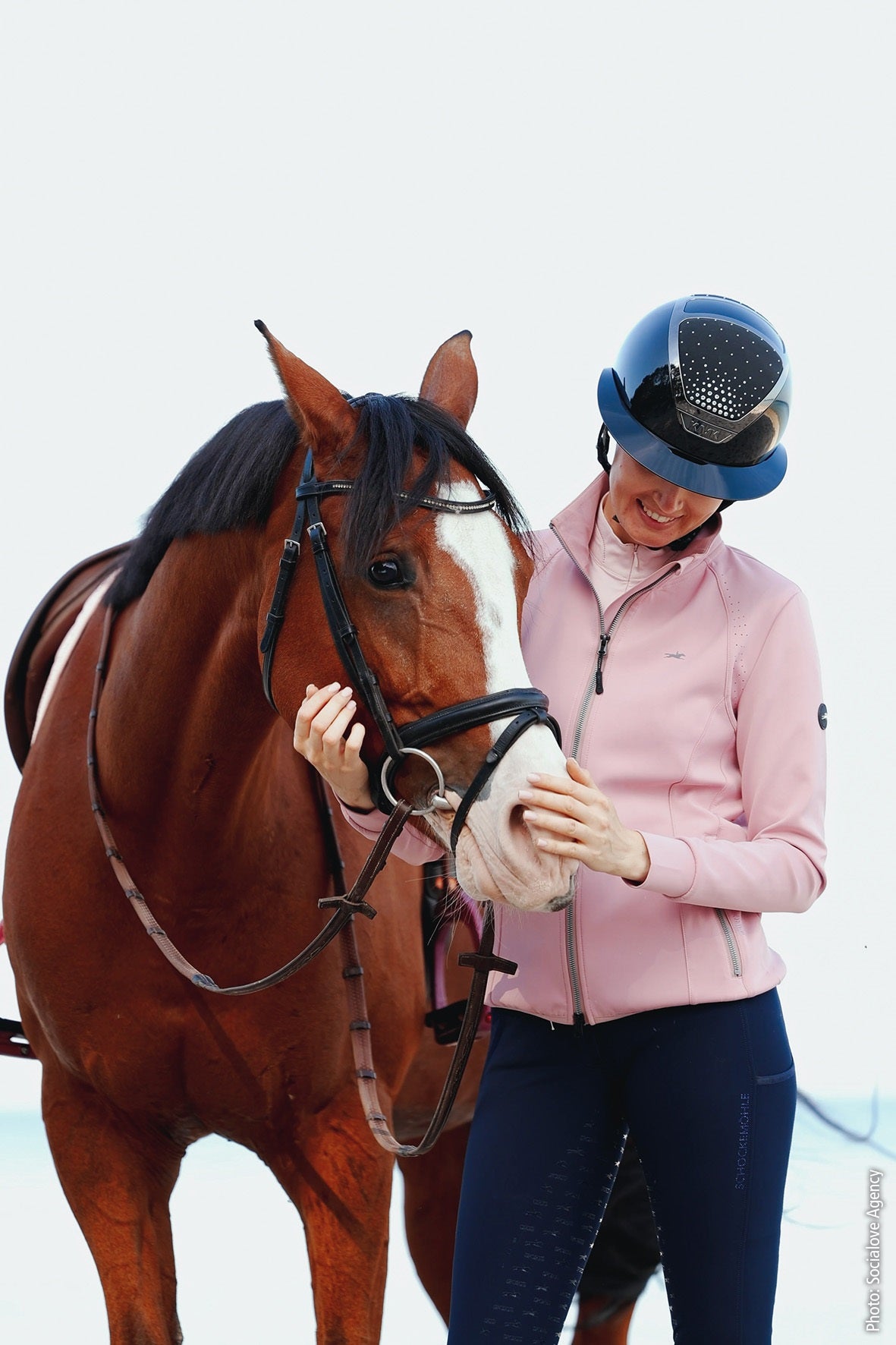 Person in equestrian attire interacting with a horse on a plain background