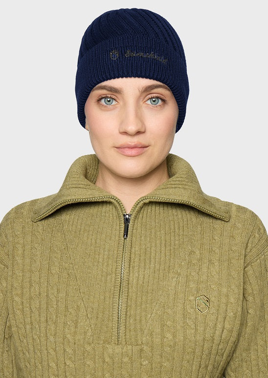 A woman wearing a navy blue ribbed knit beanie with gold embroidered branding and an olive green ribbed knit quarter-zip pullover sweater, shown against a light gray studio background.