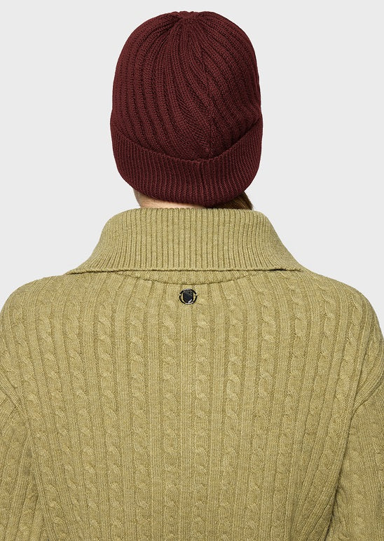 Back view of a person wearing a ribbed olive green cable-knit sweater and a dark burgundy knit beanie against a light gray background.