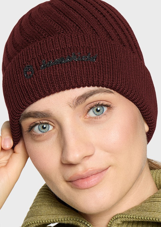 A close-up of a woman wearing a ribbed knit beanie in deep burgundy. The beanie features a small black embroidered logo on the front that reads 'Burberry'.
