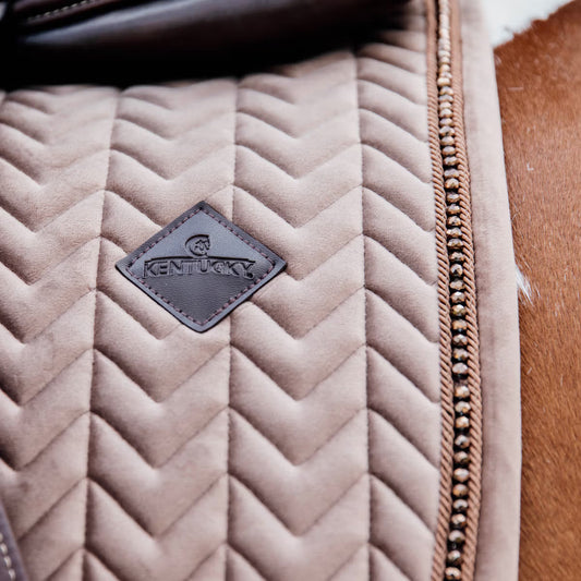 Quilted beige saddle pad with a 'Kentucky' brand patch on a brown leather background.