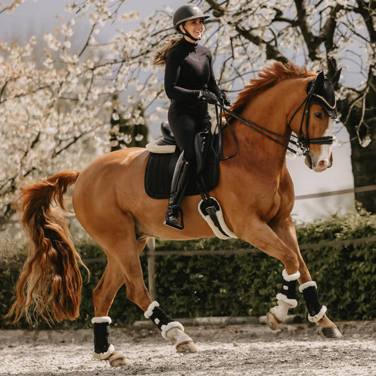 Woman riding a brown horse in an outdoor setting with cherry blossom trees.