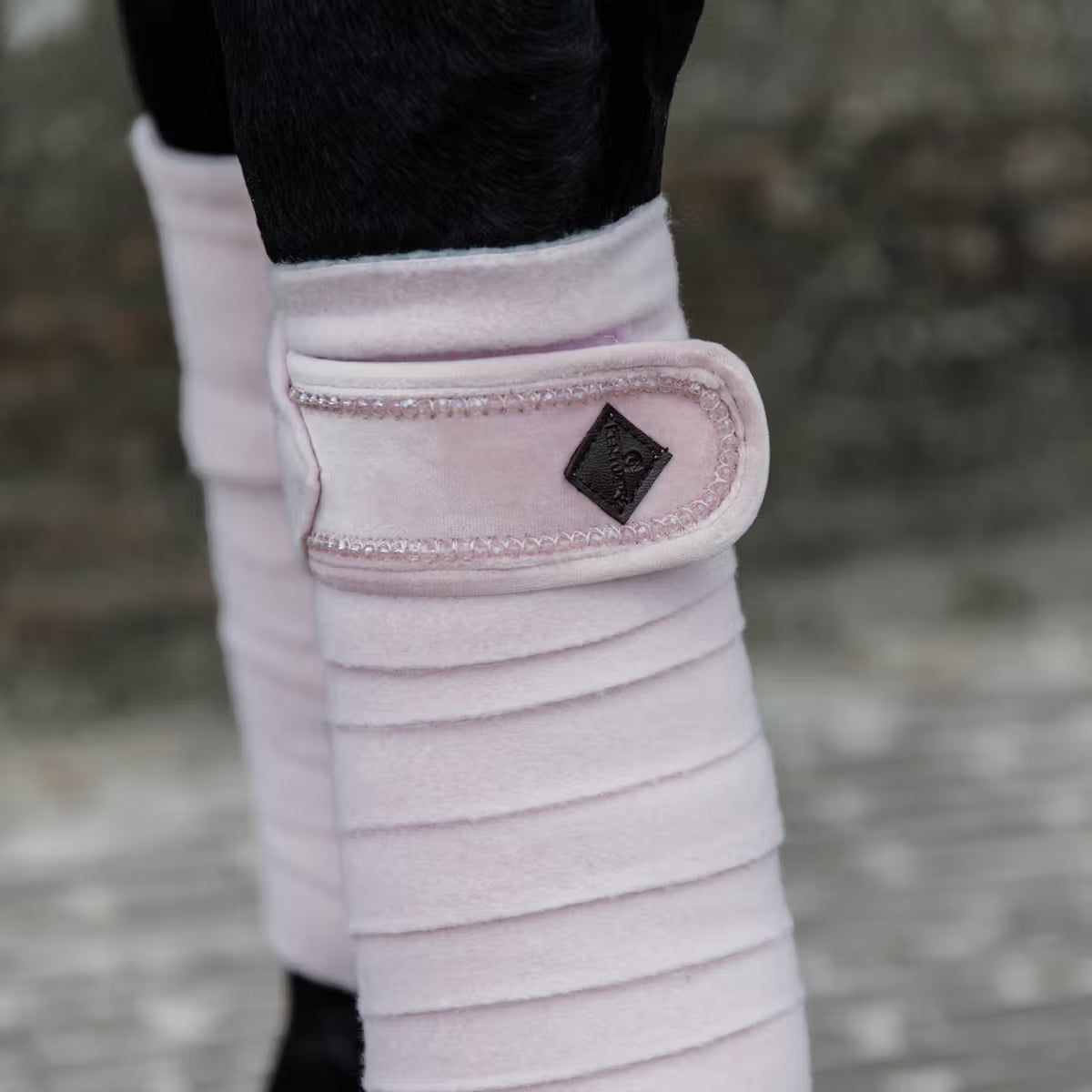 Close-up of pink protective leg wraps on a horse's legs with a blurred background.