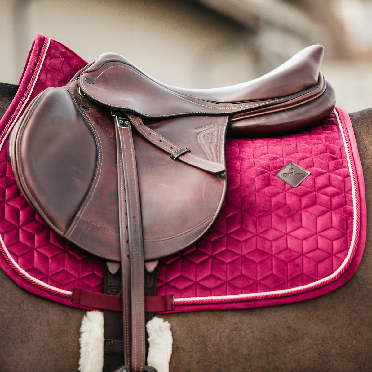 Brown leather saddle on a pink quilted saddle pad with a blurred background