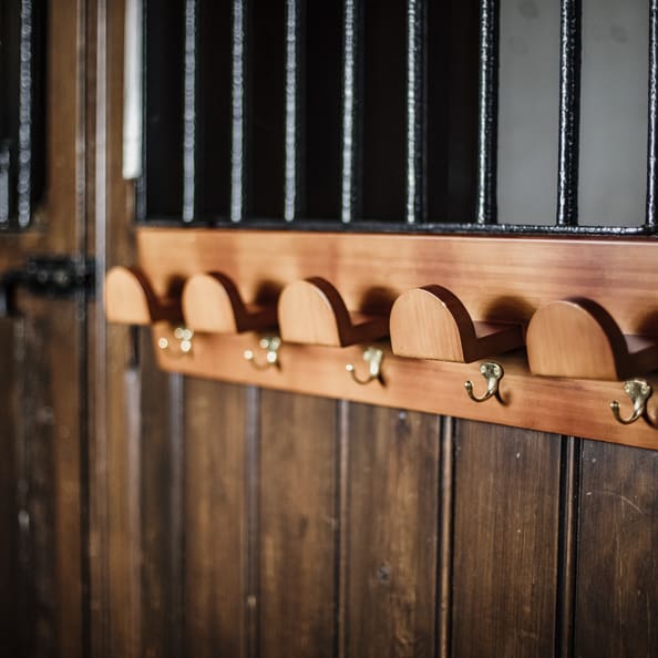 wooden bridle rack with gold hooks on it hanging on a wooden stable
