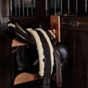 saddle sitting on wooden saddle holder, set in a dimly lit stable yard