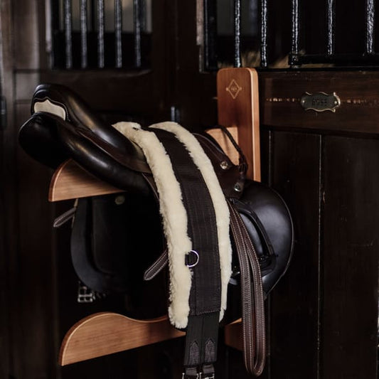 saddle sitting on wooden saddle holder, set in a dimly lit stable yard
