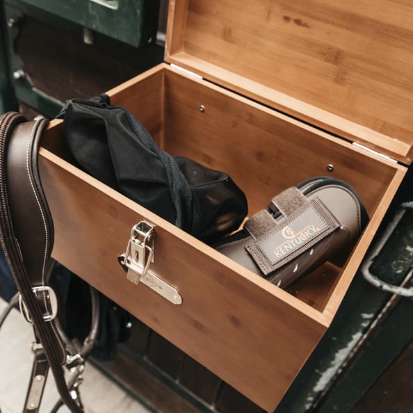 wooden grooming box with brown tendon boots inside it, hanging on a stable door