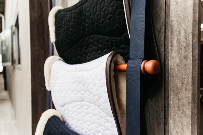 navy saddle pad holder with saddles on display in a barn