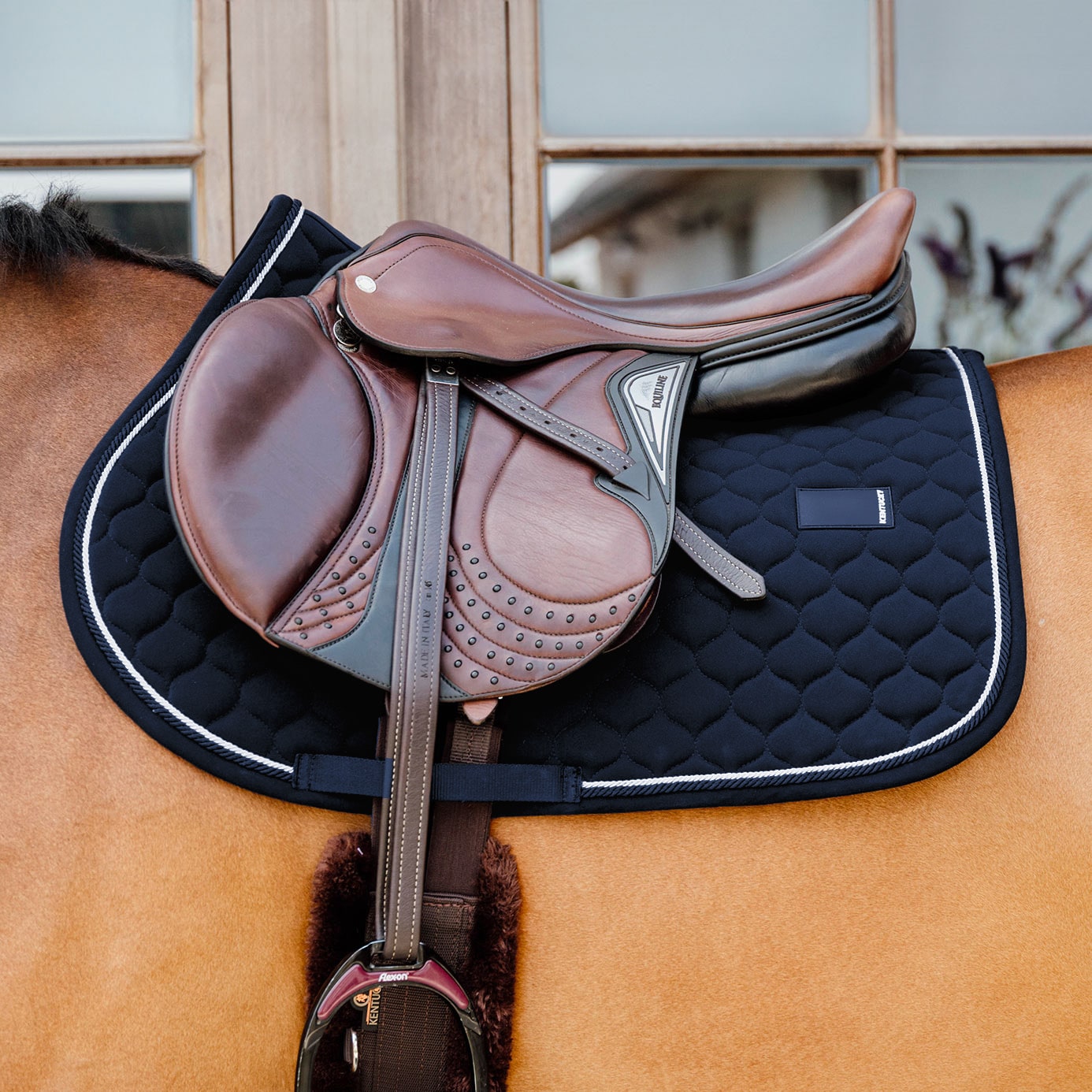 Brown saddle on a horse with a black quilted saddle pad